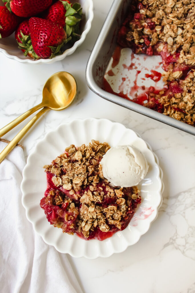 overview shot of plate with dessert, two gold spoons, a bowl of strawberries, and the baking dish