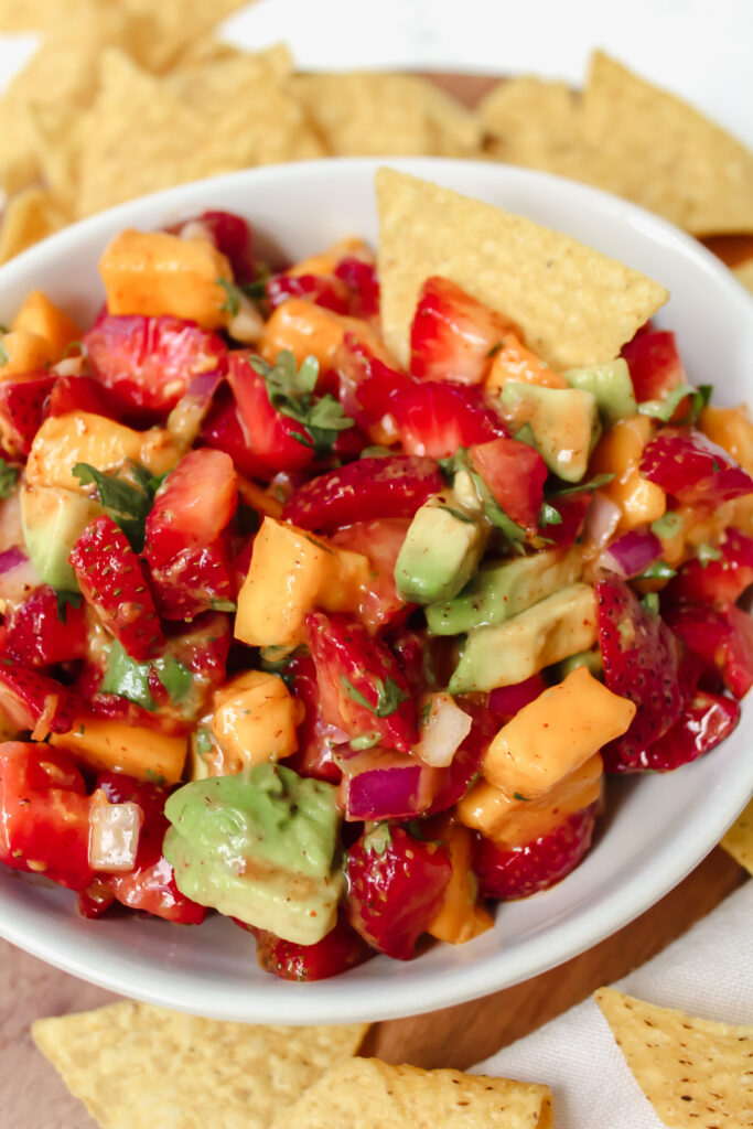 bowl of strawberry mango avocado salsa with a chip in it