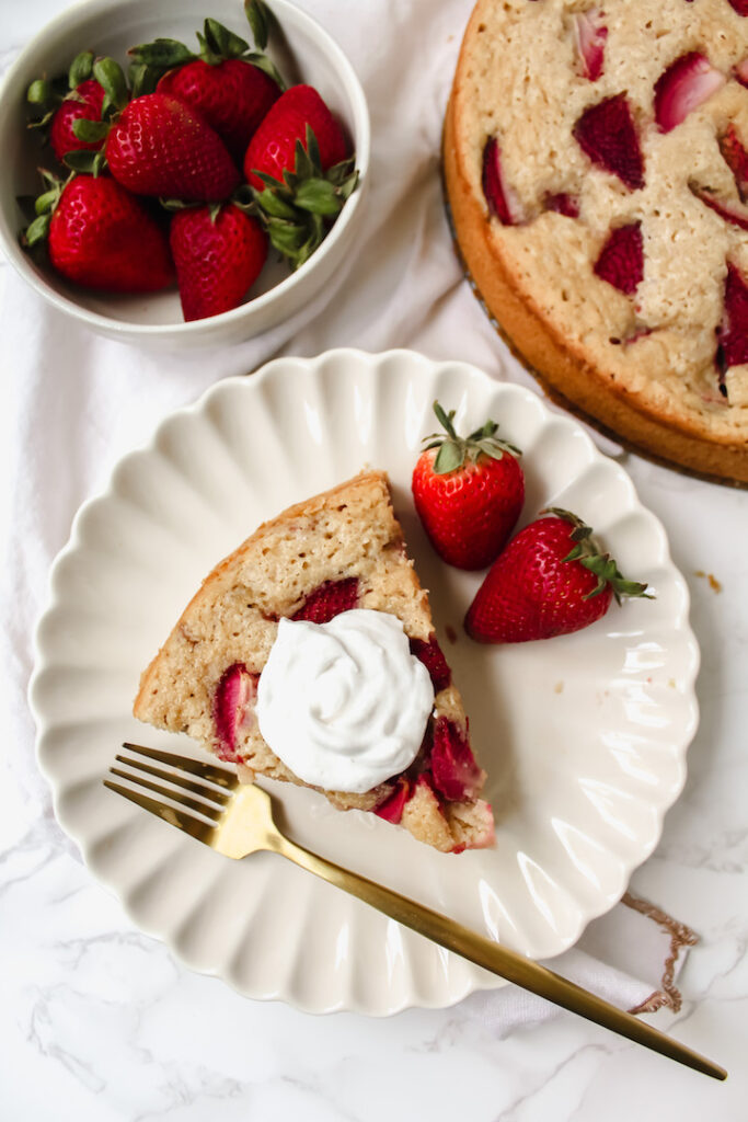 overview shot of slice of cake, bowl of strawberries, and part of the whole cake