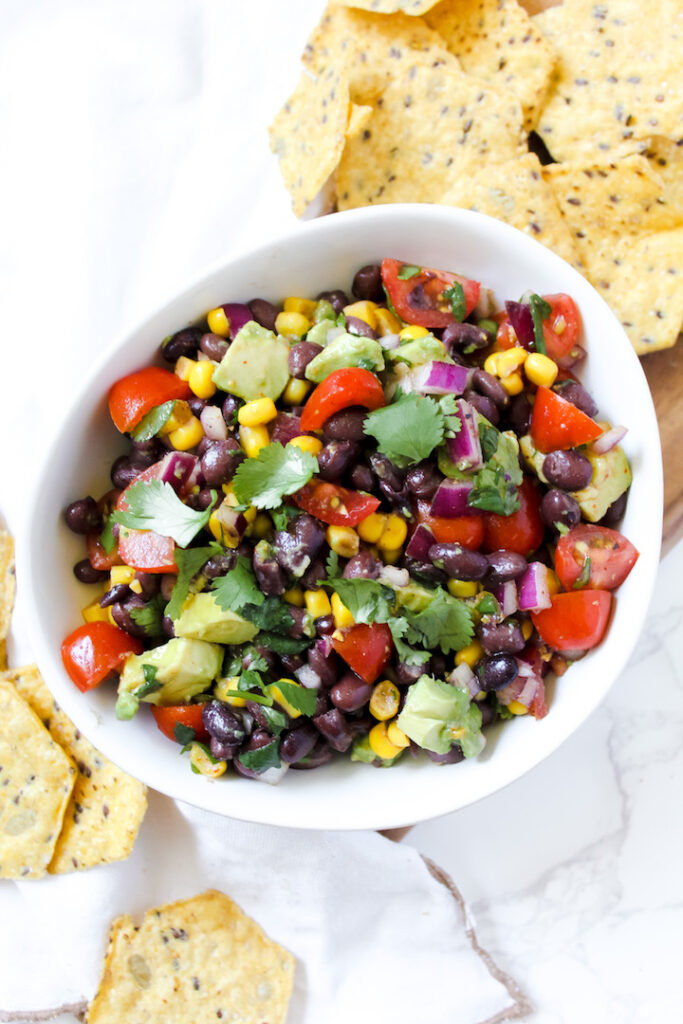 overview shot of entire bowl of black bean corn avocado salad and chip on the side