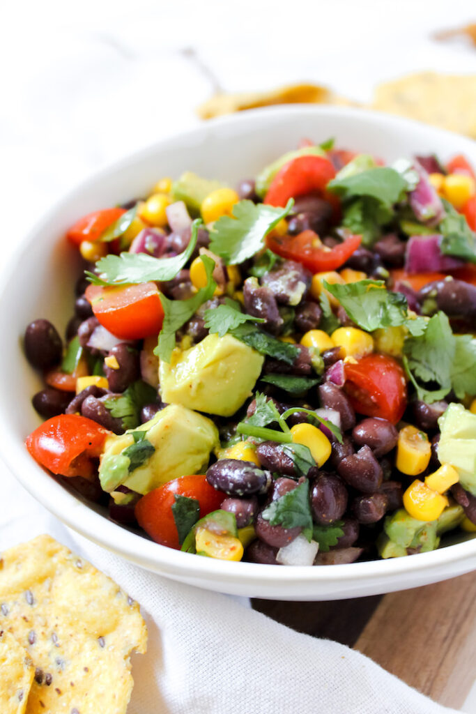 angled shot of a bowl with black bean salad in it and chips on the side