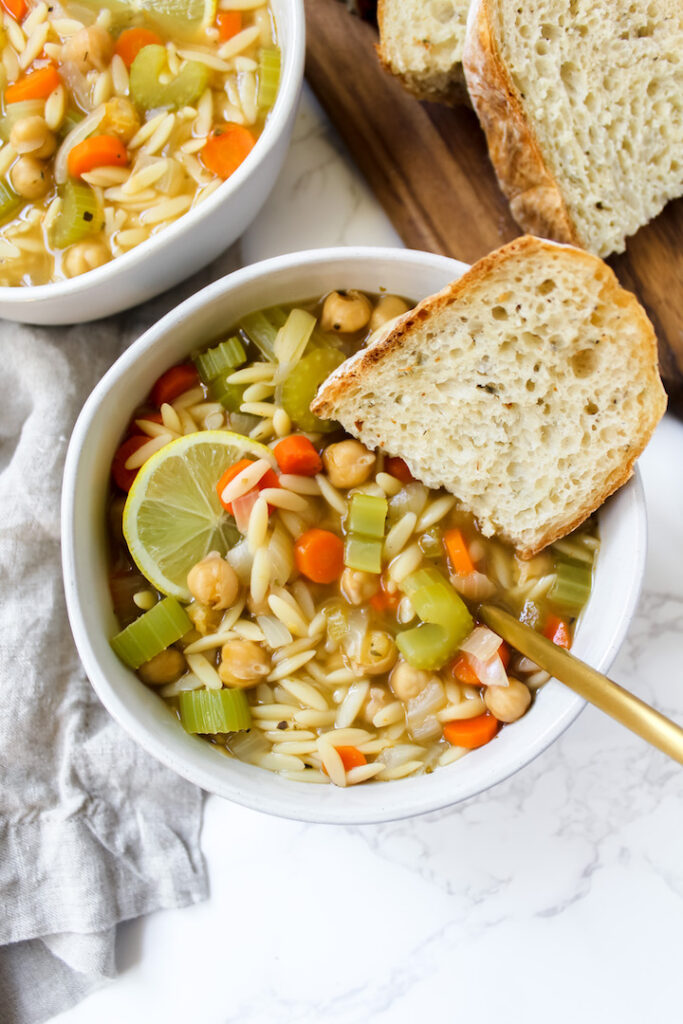 Overview shot of a slice of bread in the bowl of chickpea orzo soup