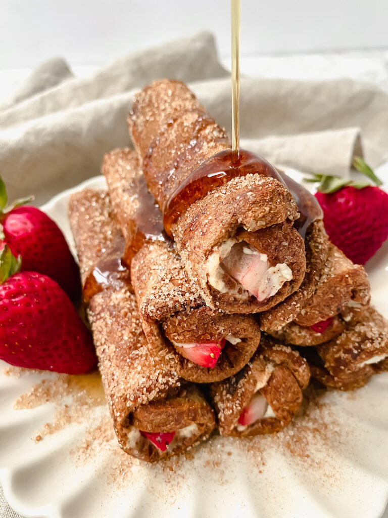 maple syrup drizzled on top of a stack of french toast roll ups