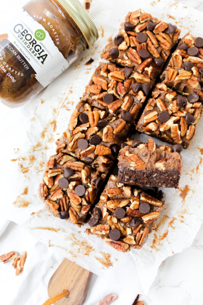 overview shot of entire turtle brownies sliced with a jar of pecan butter on the side