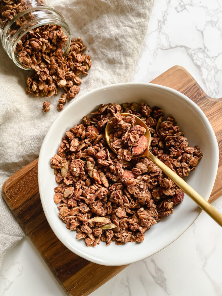 farther away shot of bowl with granola, spoon, and a jar of granola on it's side