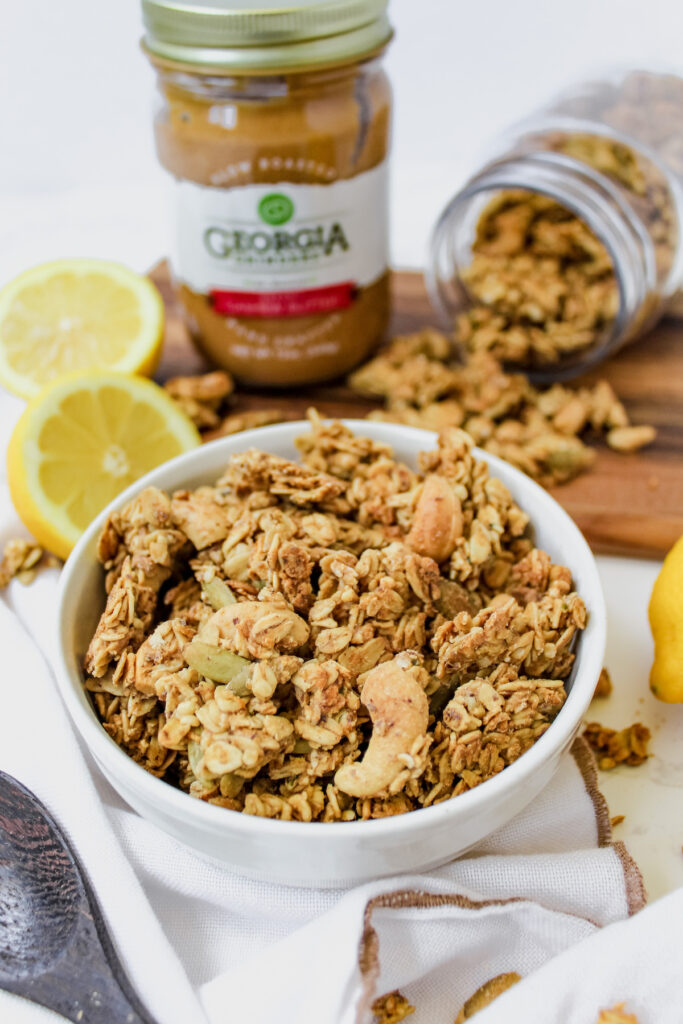 bowl of lemon cashew granola with slices of lemon in the background and jar of cashew butter