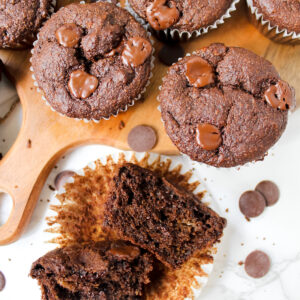 chocolate muffin split in half and whole muffins on a wooden board