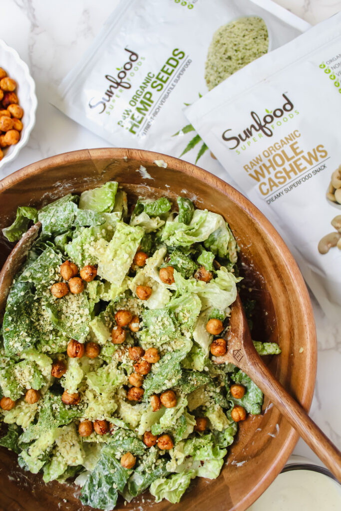 shot of bowl of caesar salad with a bag of Sunfood cashews and a bag of Sunfood hemp seeds on the side