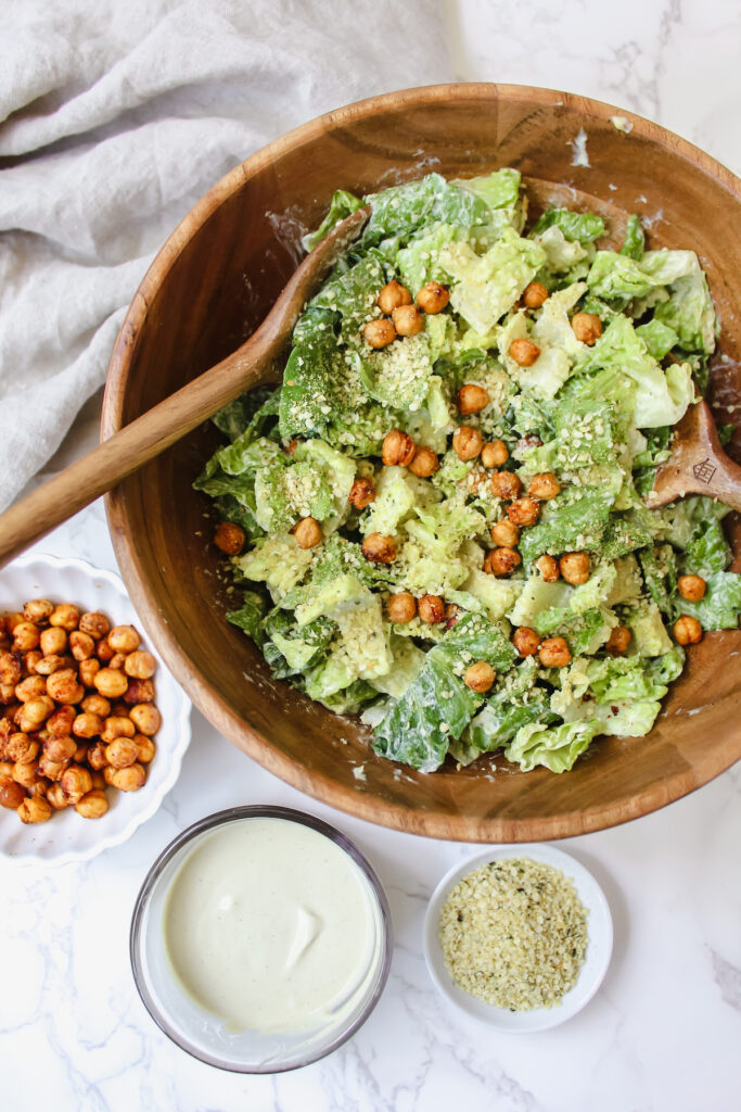 bowl of vegan caesar salad with hemp parm with 3 tiny bowls on the side