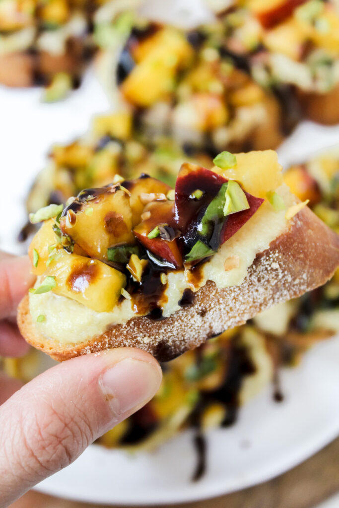 hand holding a slice of peach bruschetta with cashew ricotta