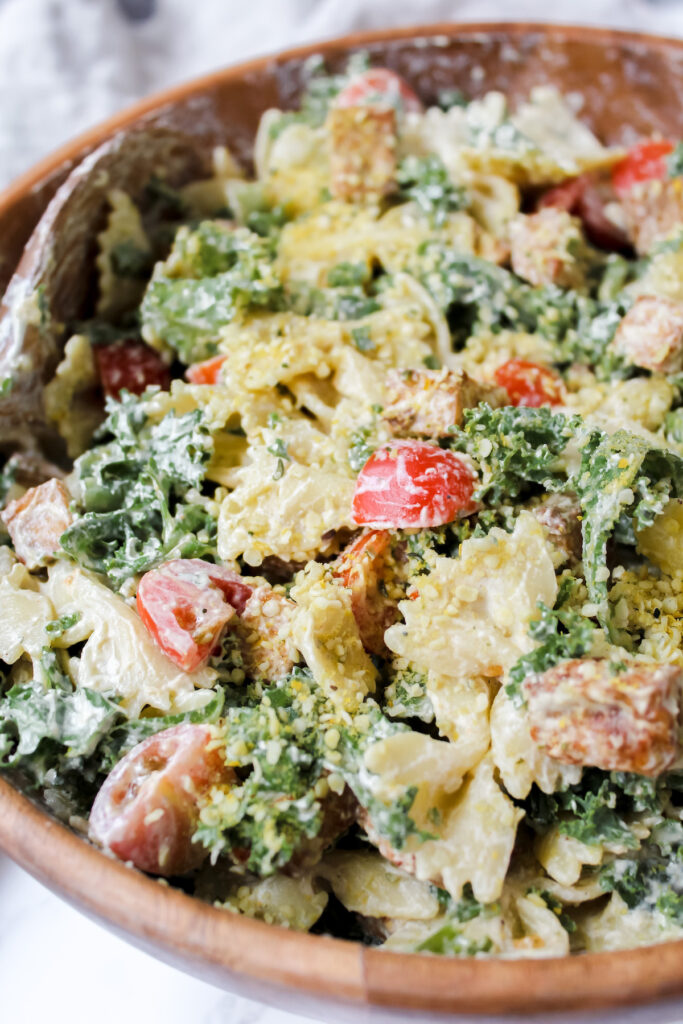 angled shot of kale caesar pasta salad in wooden bowl 