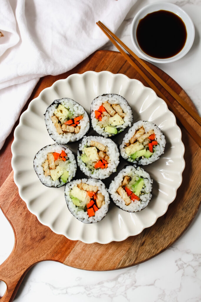 overview of plate of teriyaki tempeh sushi rolls with chopsticks and a bowl of soy sauce on the side