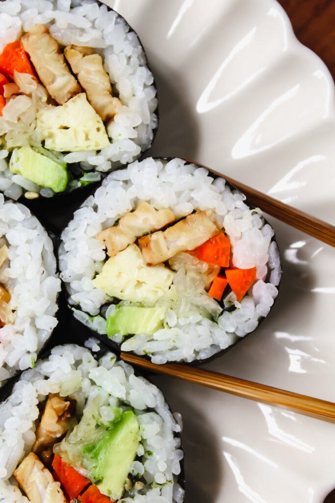 chopsticks about to lift a slice of the teriyaki tempeh sushi roll