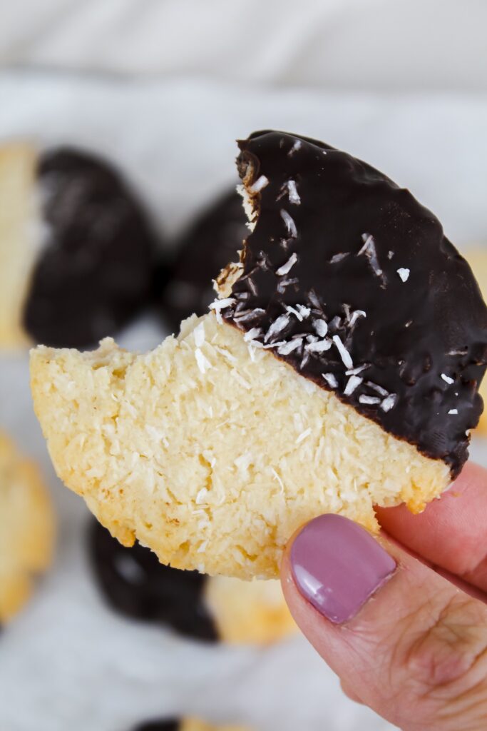 hand holding a chocolate dipped coconut cookie with a bite taken out of it