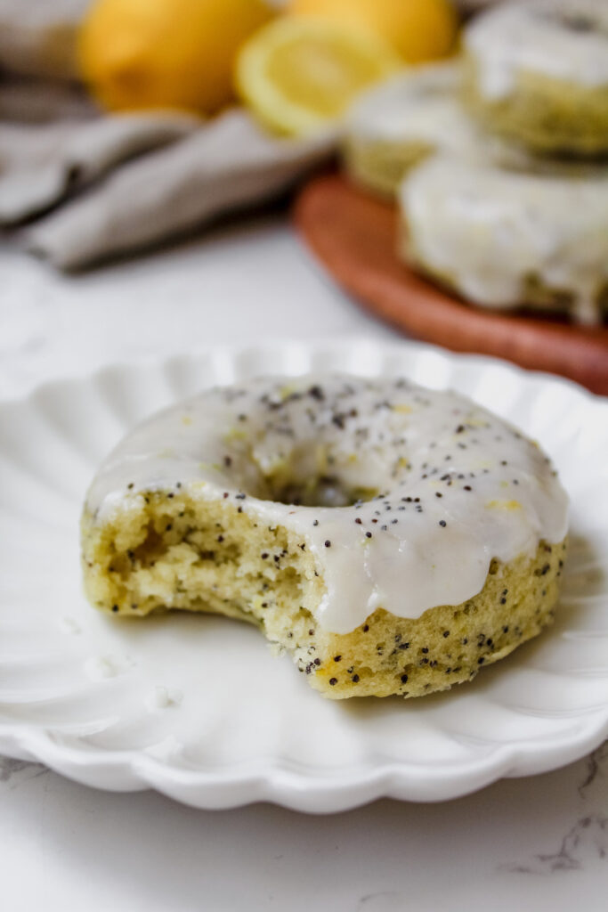 close up shot of lemon poppy seed donut on a plate with a bite taken out