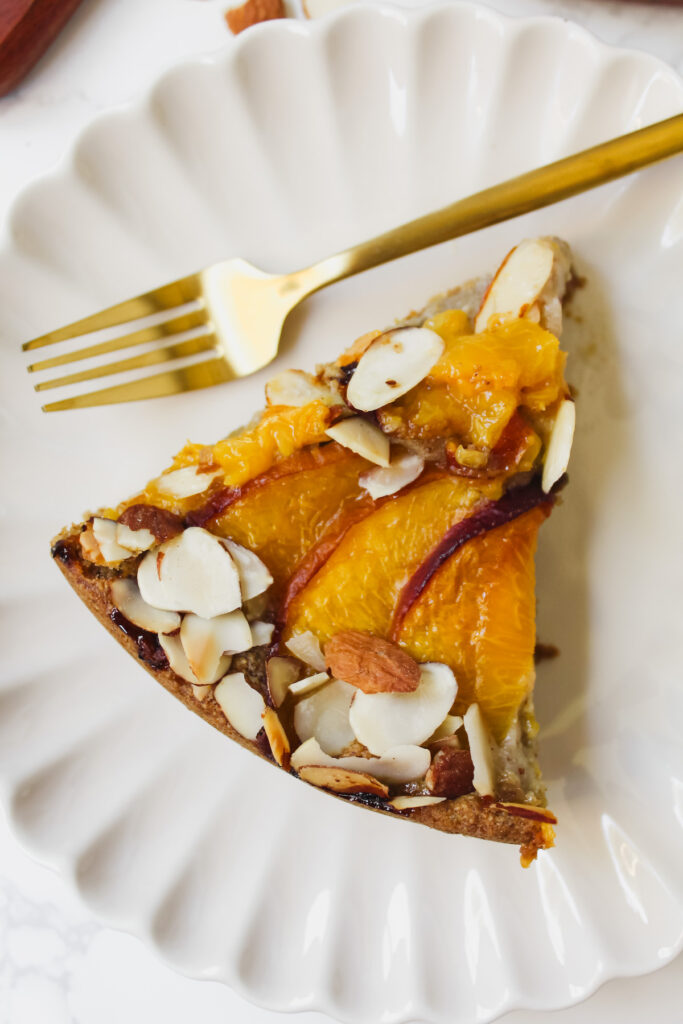 slice of almond peach oat cake on a plate with a gold fork next to it