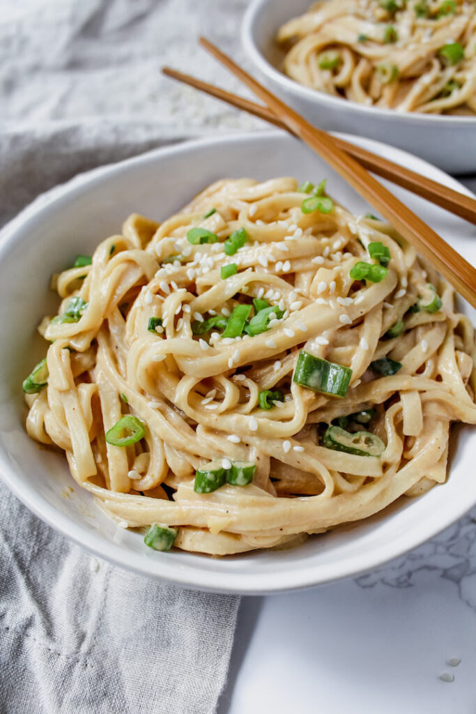 close up angled shot of noodles with sesame seeds and scallions on top