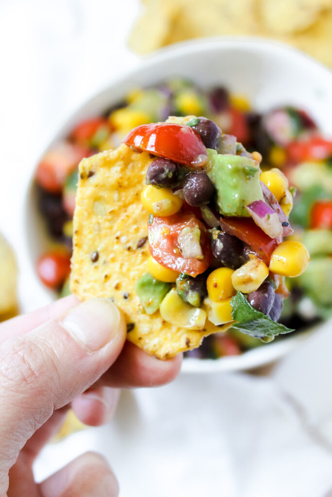 hand holding a chip with black bean corn avocado salad on it
