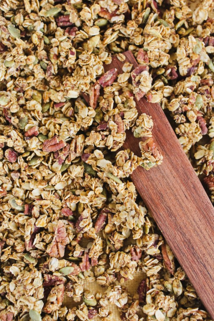 pumpkin pecan granola on a pan with a wooden spatula