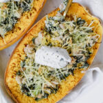creamy white bean and kale stuffed spaghetti squash with a dollop of cream cheese on top and a fork in it