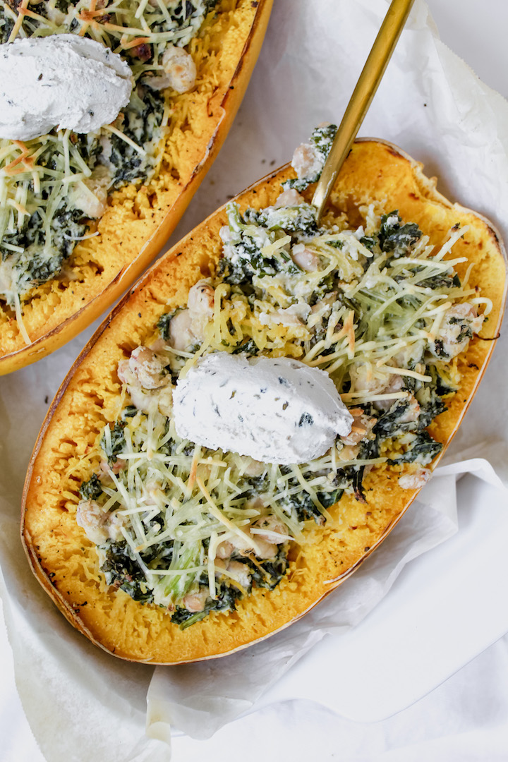 creamy white bean and kale stuffed spaghetti squash with a dollop of cream cheese on top and a fork in it