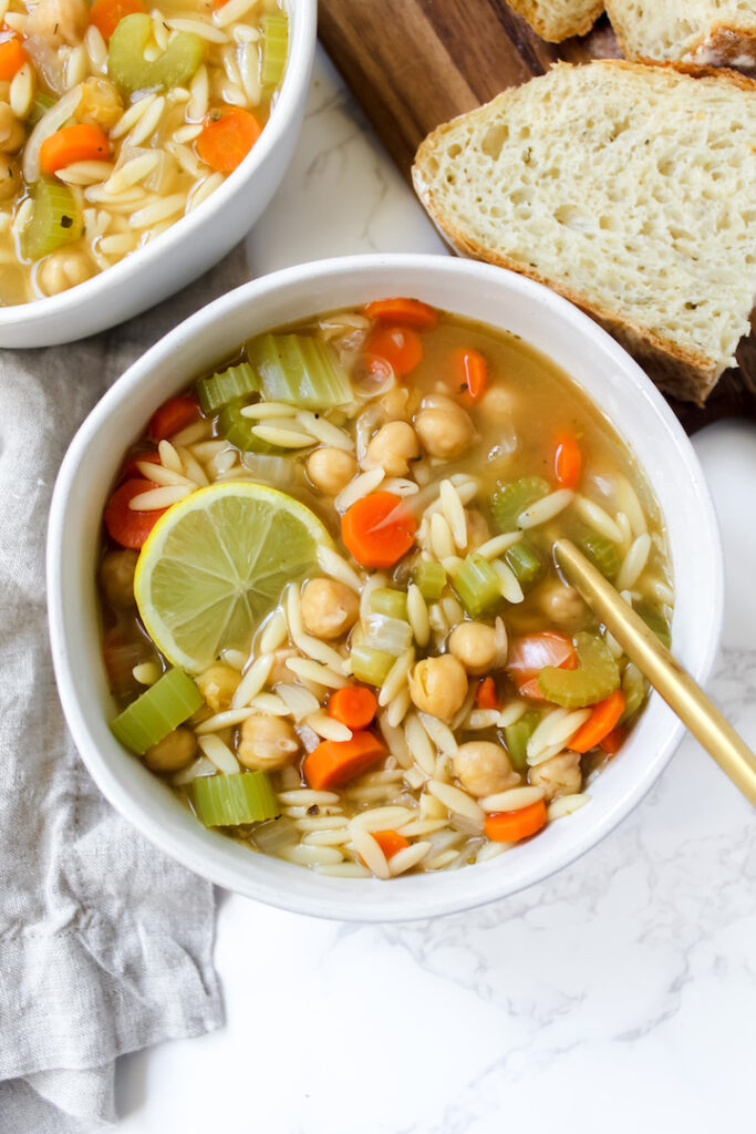 overview shot of bowl of orzo soup with bread on the side