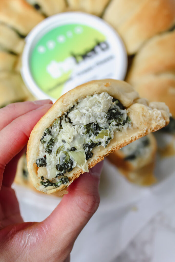 close up shot of hand holding a slice of the spinach artichoke crescent ring