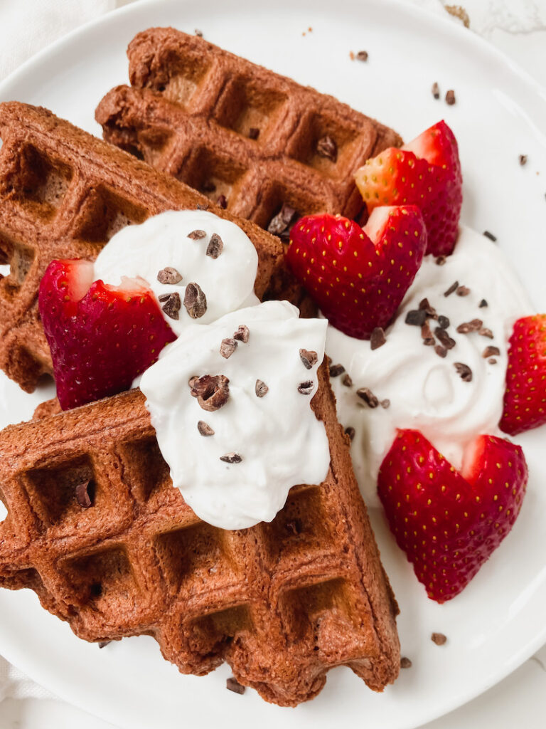 close up of healthy red velvet waffles with yogurt, cacao nibs, and strawberries on top