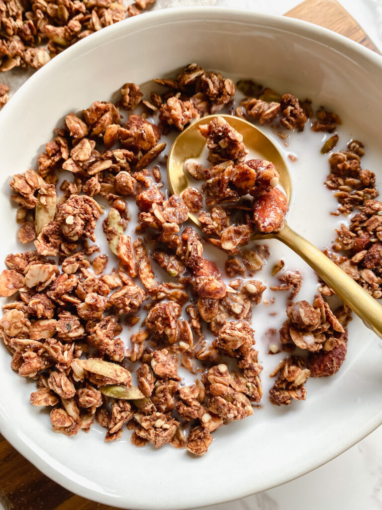 peanut butter cacao granola with milk and a gold spoon
