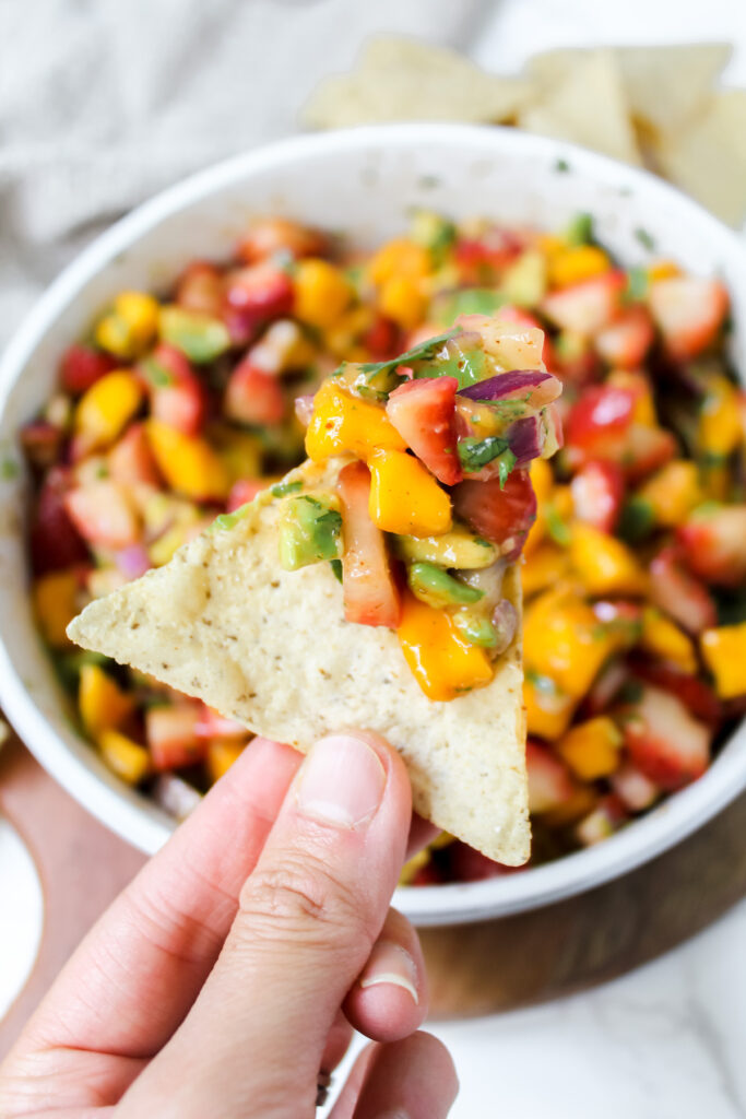 hand holding a chip with strawberry mango avocado salsa on it
