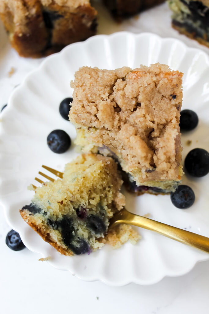 close up shot of a slice of blueberry coffee cake with a bite on a fork