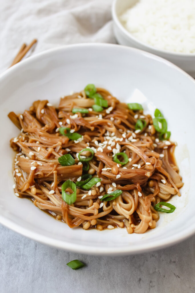 close up angled shot of enoki mushrooms in a bowl with sesame seeds and green onions on top