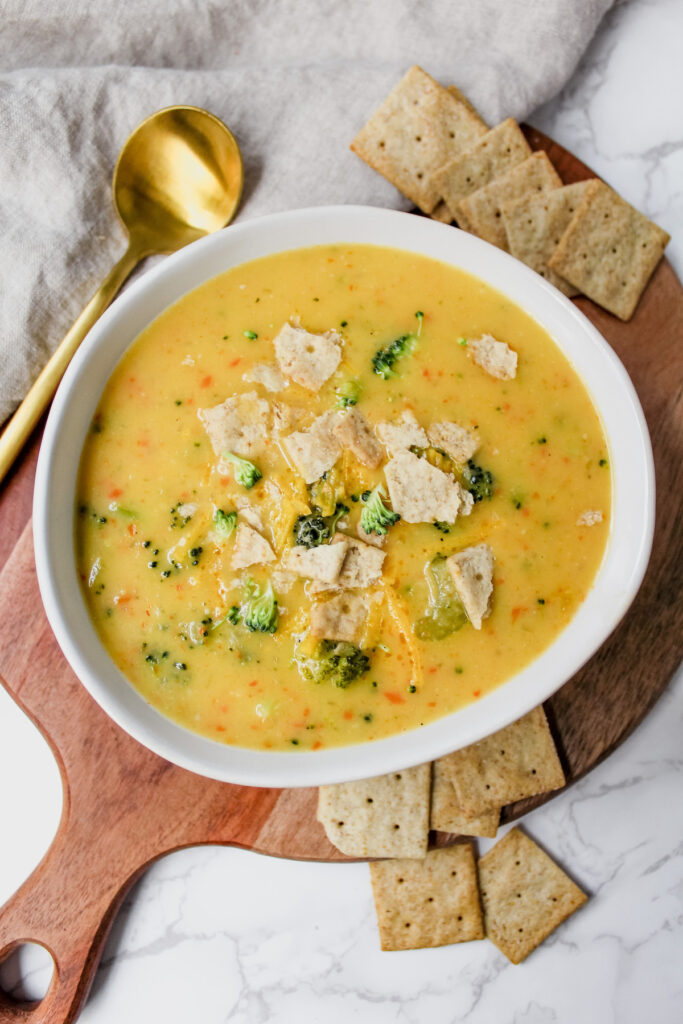 overview shot of entire bowl of broccoli cheese soup with crackers on the side