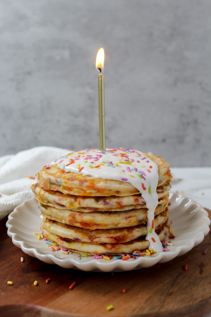 shot of stack of vegan birthday cake pancakes with a candle in the middle