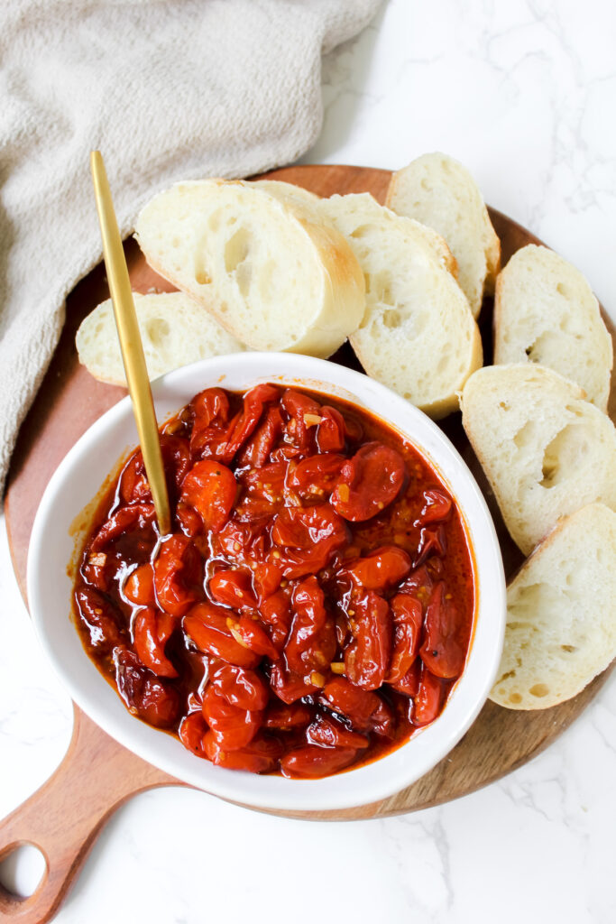 overview shot of a bowl of garlic gochujang roasted cherry tomatoes with sliced bread on the side