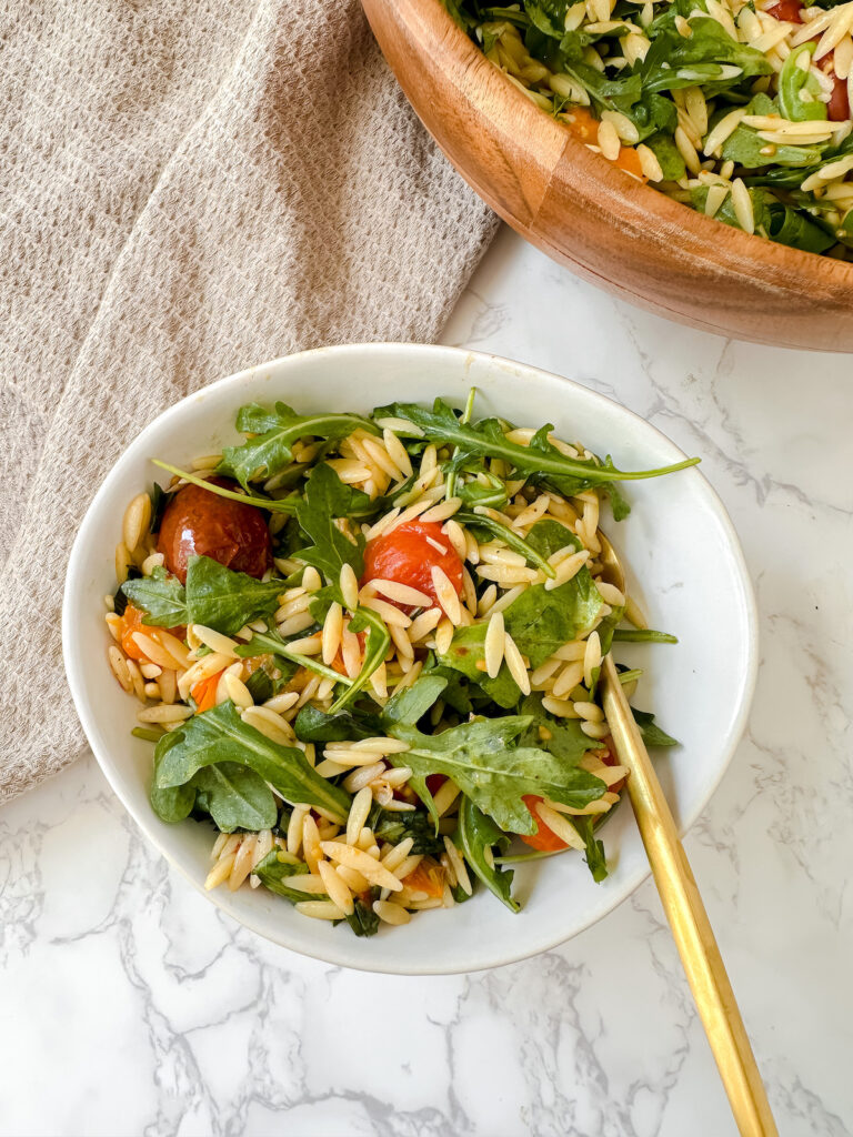 overview shot of orzo salad in a white bowl with a gold fork