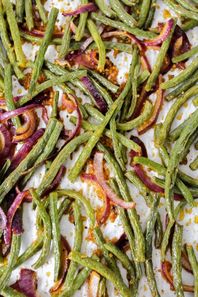 shot of roasted green beans and red onions on a sheet pan