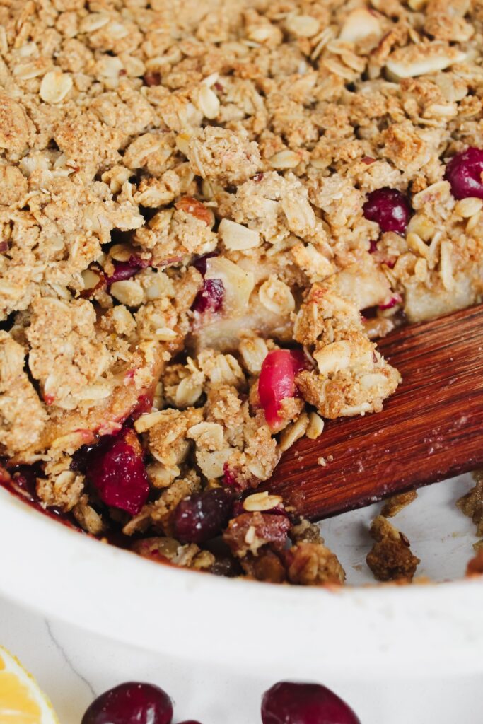 close up of the inside of the orange cranberry apple crisp with spatula in the pan