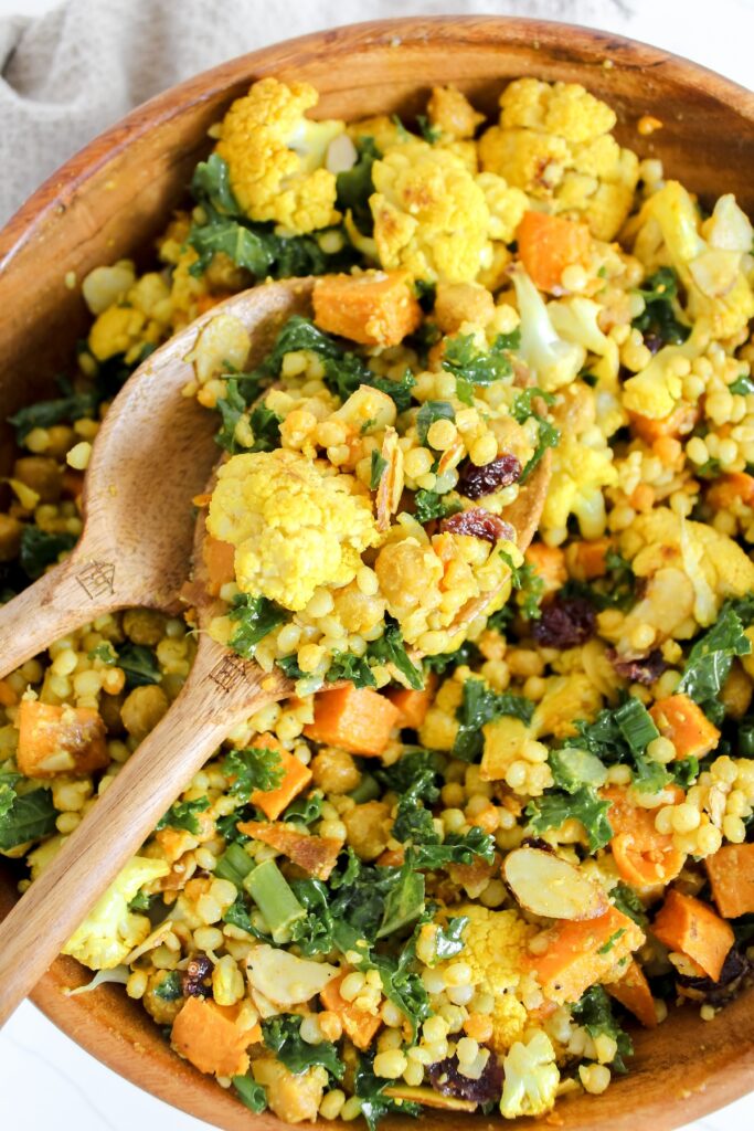 curry roasted cauliflower couscous salad in a wooden bowl with salad serving spoons in it