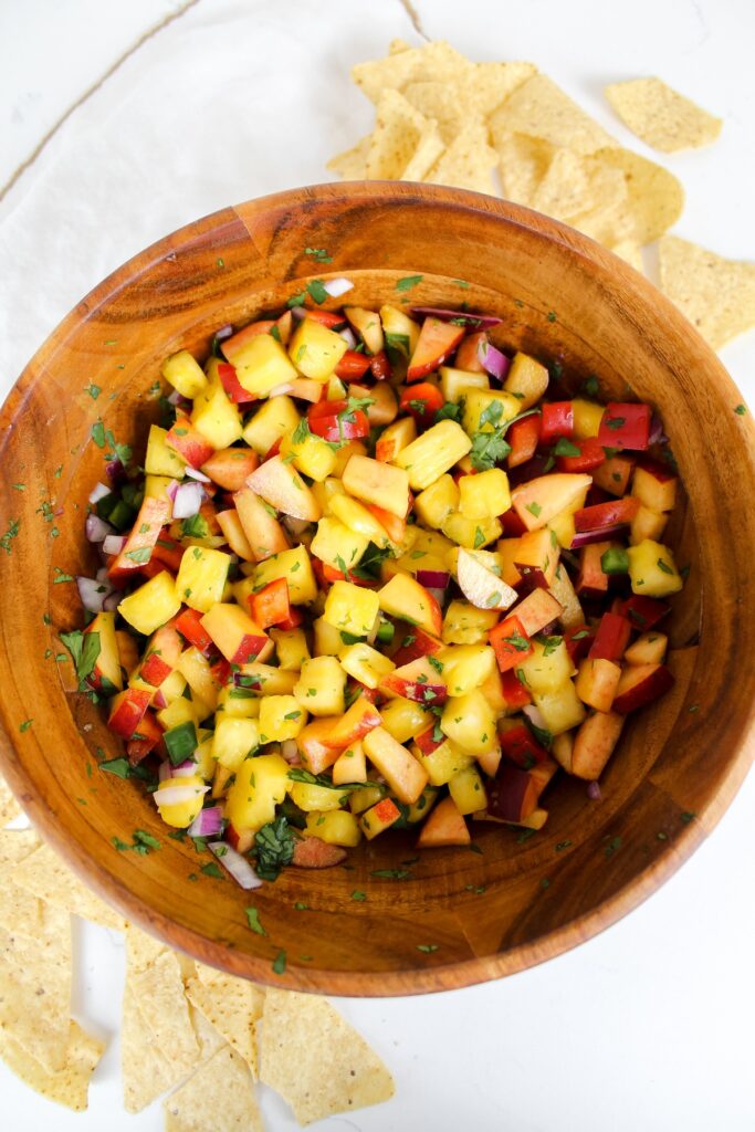 pineapple peach salsa in a wooden bowl with chips on the side