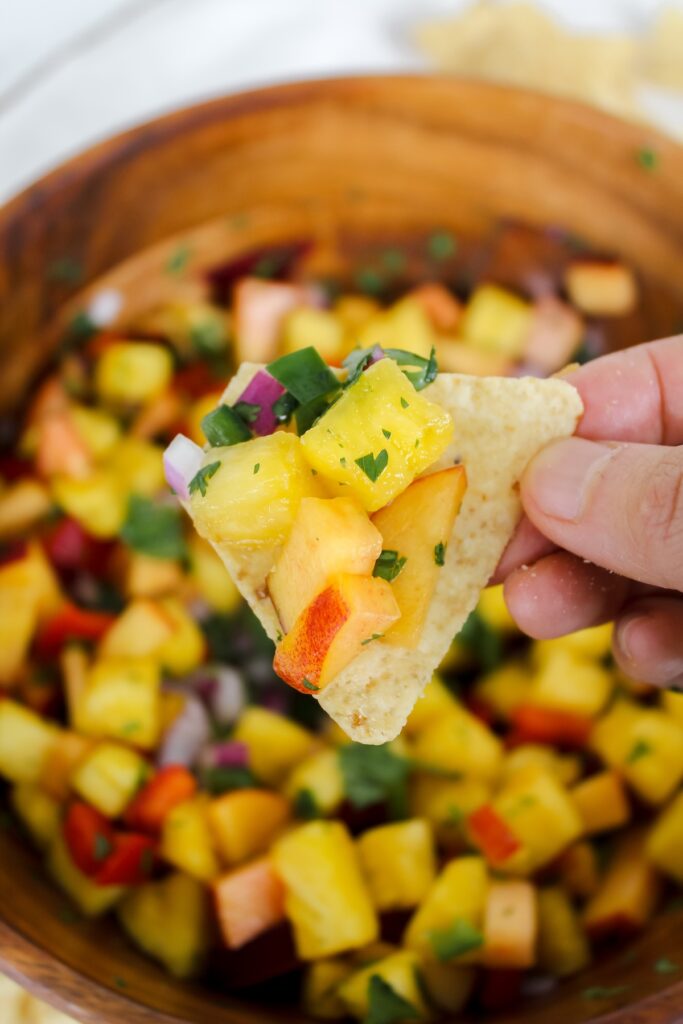 hand holding chip with pineapple peach salsa on it