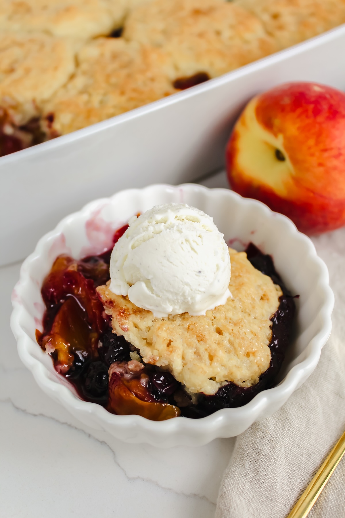 close up shot of cobbler in a white bowl with ice cream on top
