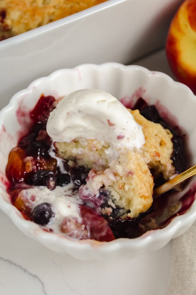 a spoon in a bowl of vegan blueberry peach cobbler