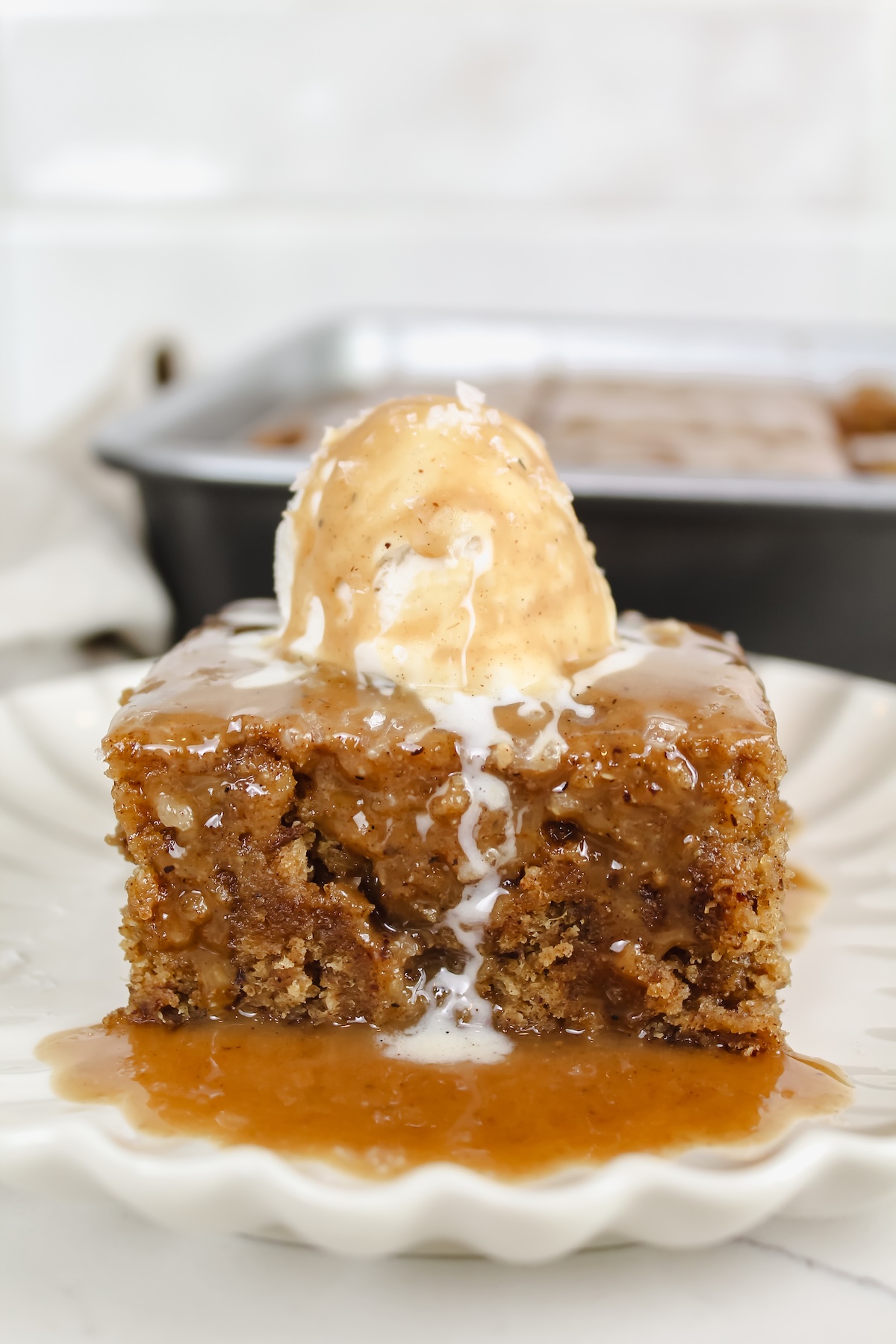a slice of banana sticky toffee pudding on a plate with ice cream on top