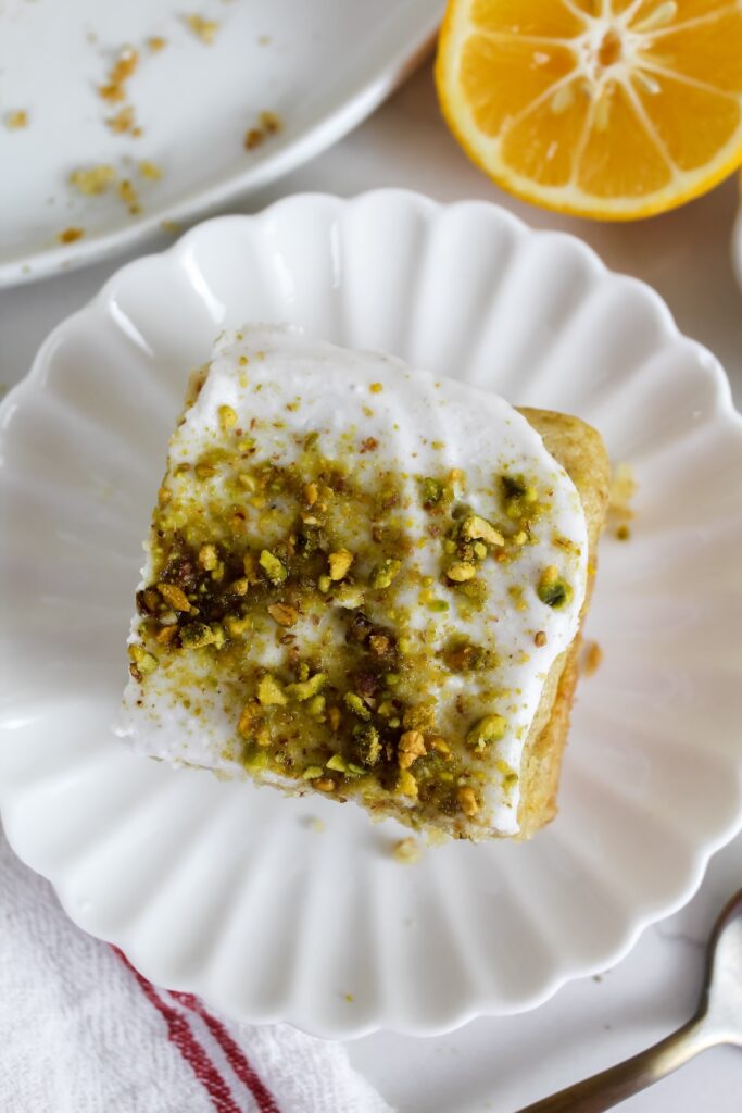 close up of a slice of lemon pistachio olive oil cake on a white plate