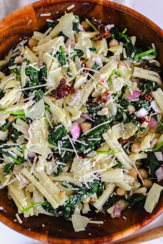 spinach artichoke pasta salad in a wooden bowl