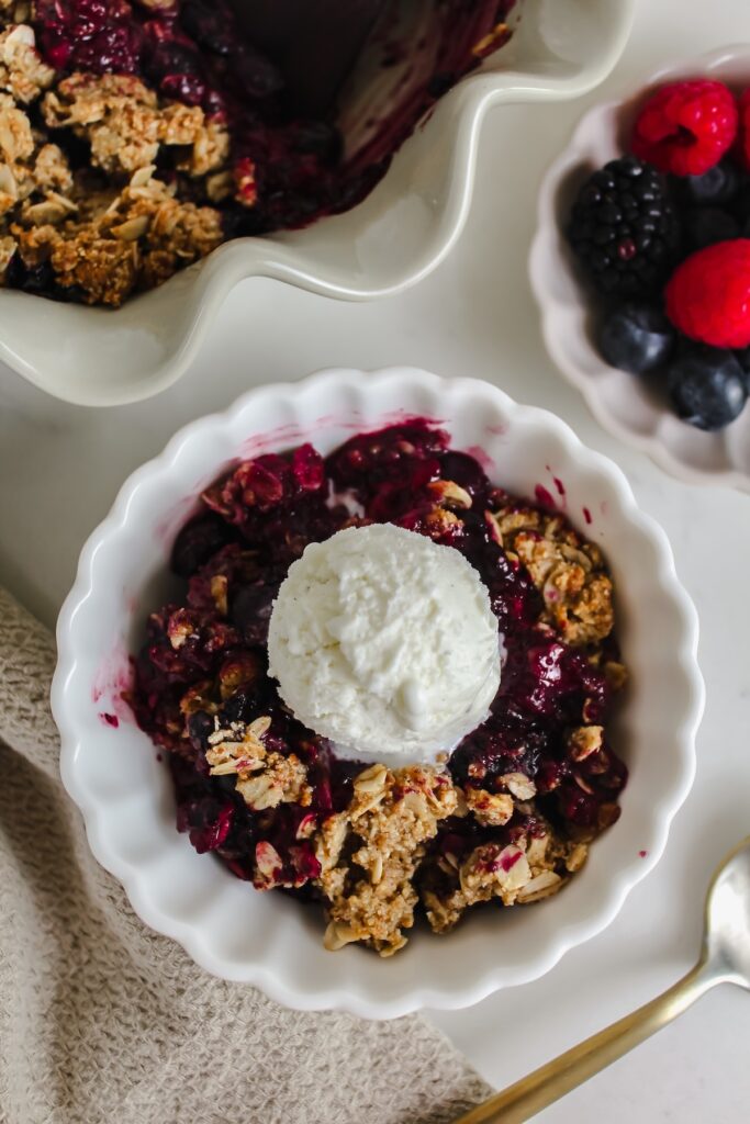overview shot of white bowl with healthy triple berry crisp and ice cream