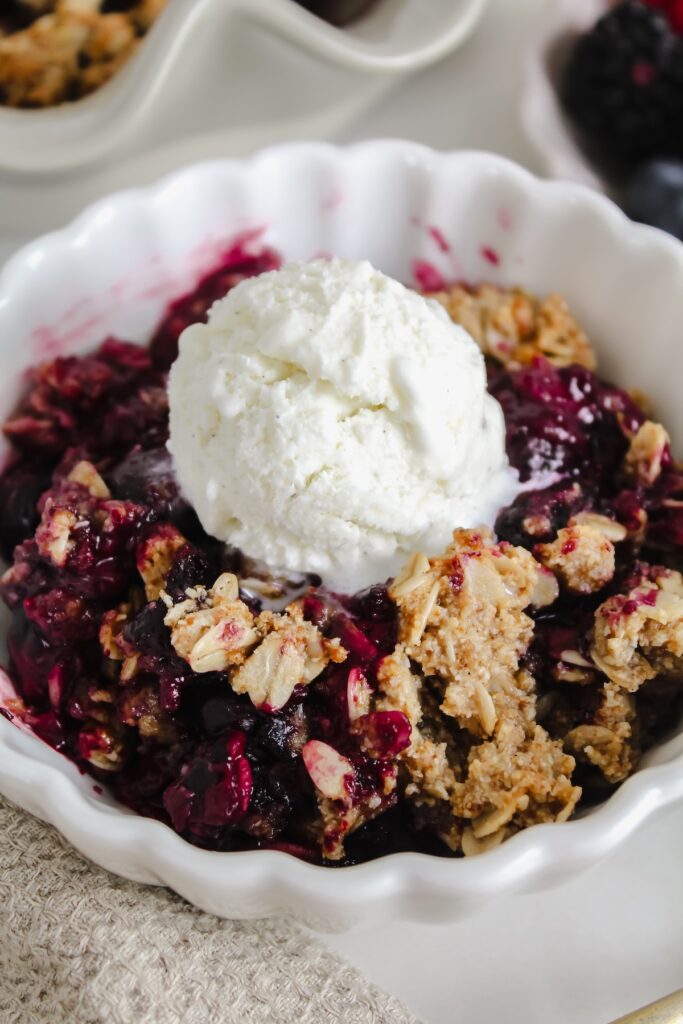 angled close up shot of bowl with berry crisp and ice cream on top